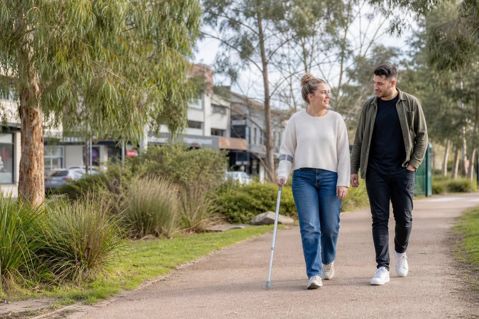 An adult participant walking through a leafy Melbourne community space with support nearby